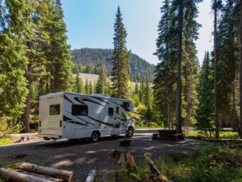 Beautiful campsite in the mountains with an RV and wooden bench.